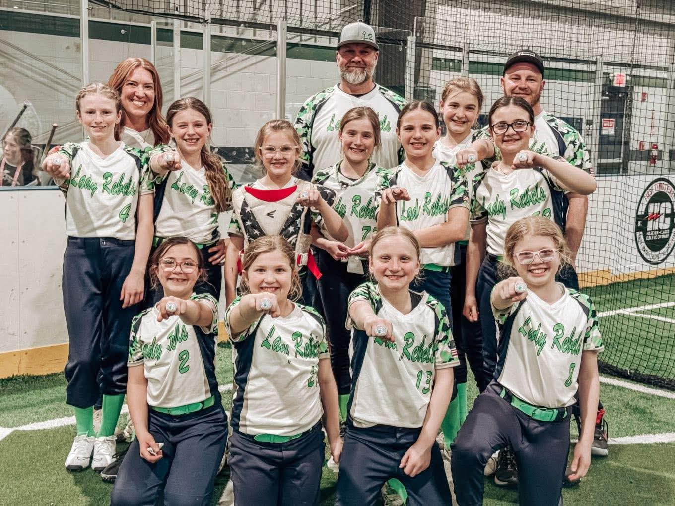 A softball team with coaches holding their tournament rings in celebration.