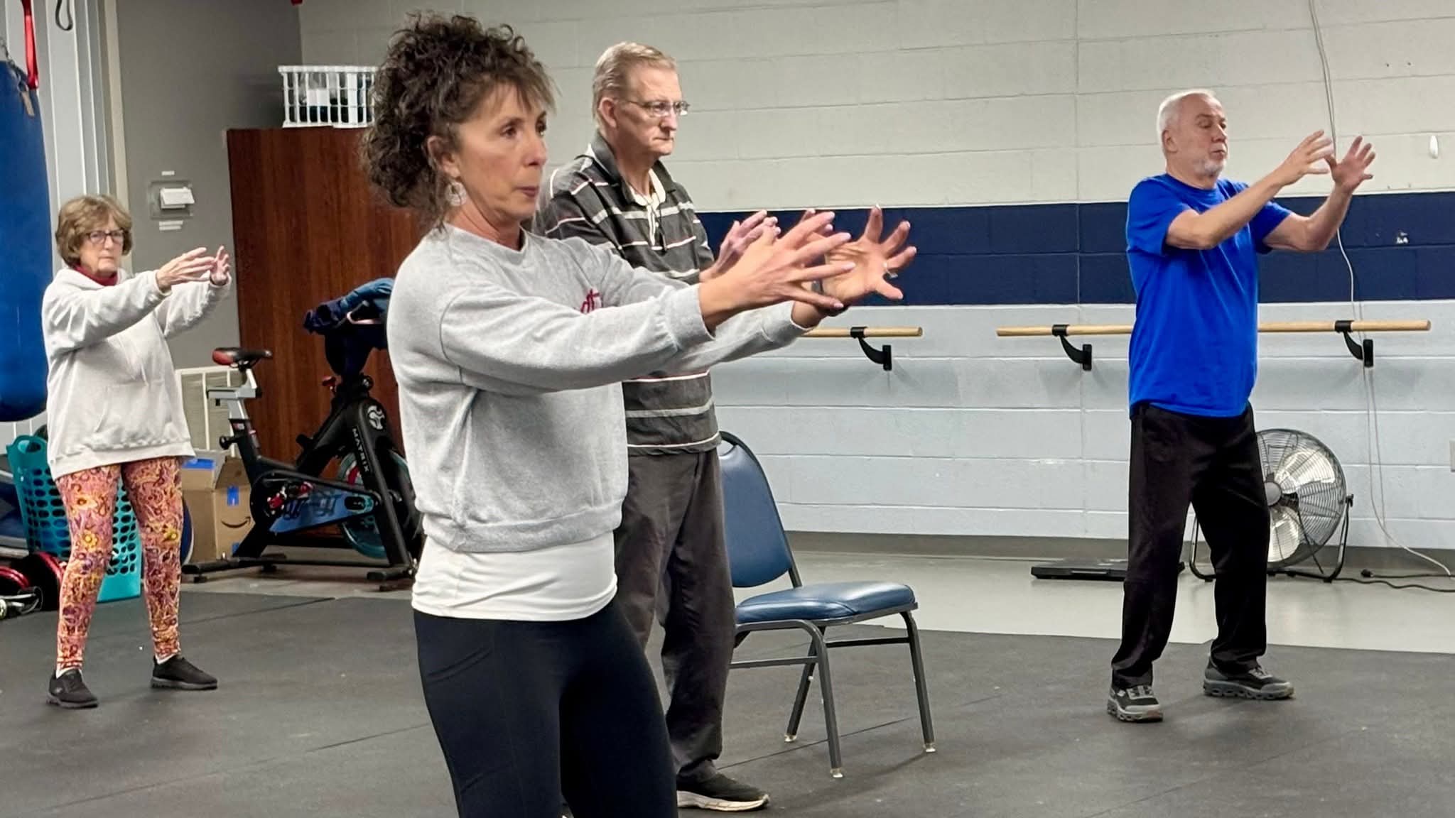 Instructor leading tai chi class with people in attendance following the instruction